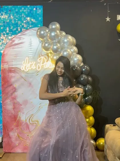 Dancing with joy at her 27th birthday party. The vibrant decor with a "Let's Party" neon sign and sequin wall creates the perfect backdrop for a lively celebration.