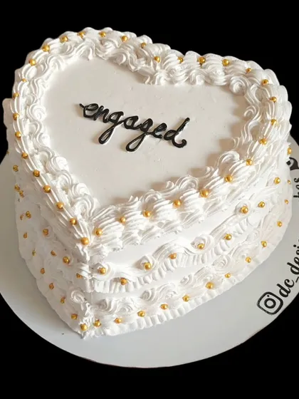 A classic white heart-shaped cake for an engagement. The simple piping and gold pearls create a timeless and elegant look.