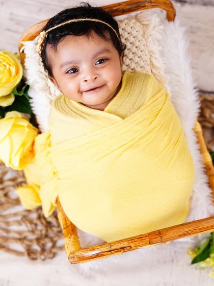 A beautiful smiling newborn, wrapped in a sunny yellow swaddle and surrounded by matching flowers. Her happy expression is everything!