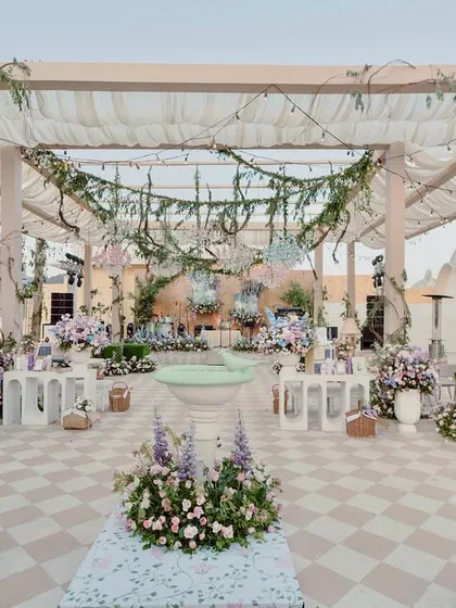 A wide view of a terrace garden we designed at The Leela Palace, Jaipur. The space combines checkered flooring, lush floral arrangements, and interactive stations under a canopy of greenery and lights, creating a whimsical, multi-layered experience for guests.