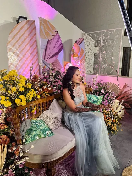 A beautiful wide shot of the client at her mehndi event, seated amidst a stunning floral decor setup.