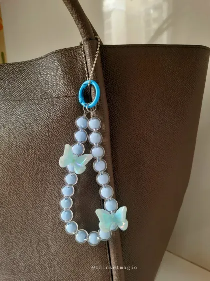 A beautiful sky blue beaded bag charm with iridescent butterfly accents. The matching blue clasp completes this dreamy, cohesive look.