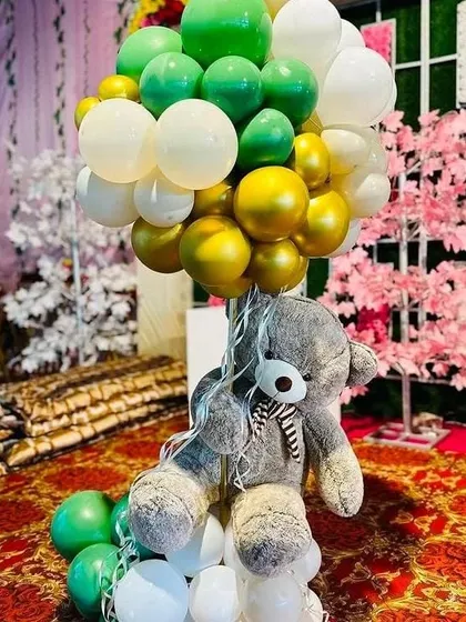 I make sure the theme carries through the entire venue. This is a table centerpiece with a teddy bear holding a bunch of green, white, and gold balloons, matching the main stage decor.