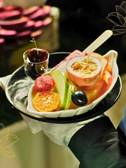 An exotic fruit platter served with impeccable style. A gloved hand presents a curated selection including passionfruit, apple, and cherries, showcasing our premium service.