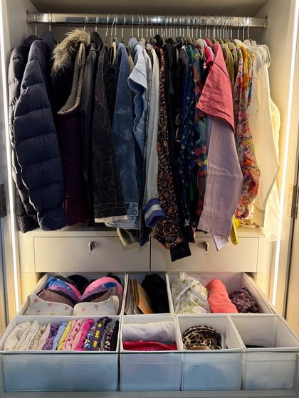 A wardrobe where hanging clothes are placed above drawers filled with neatly organized smaller items. The integrated lighting makes everything inside visible and accessible.