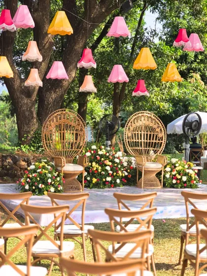 The main seating area for the 'Artistic Atelier' Haldi, featuring peacock chairs, colorful hanging lampshades, and a backdrop of flowers.