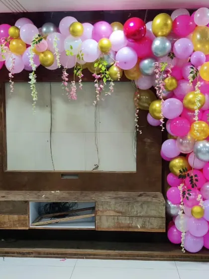 A vibrant balloon garland in shades of pink and yellow, designed to frame a TV unit for a welcome home party.