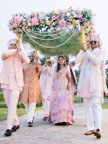 The bride being escorted to her wedding under a beautiful 'phoolon ki chaddar' held by her brothers, a traditional and emotional moment.