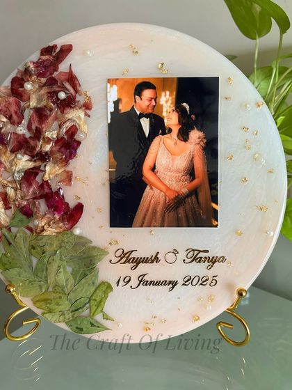 This circular plate has a soft pink background with preserved red petals and green leaves arranged on one side. It's a beautiful example of a more minimalist design.