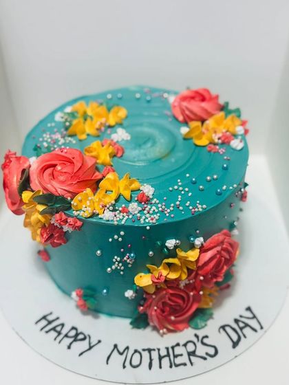 A vibrant teal cake decorated with colorful buttercream flowers for Mother's Day.