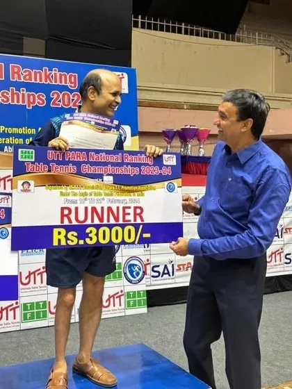 A smiling Gajanan Parmar receives his prize money check on the podium, celebrating a successful tournament at the PARA National Rankings.