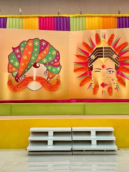A quirky and colorful stage backdrop for a Haldi or Mehendi, featuring fun illustrations decorated with real marigold flowers.