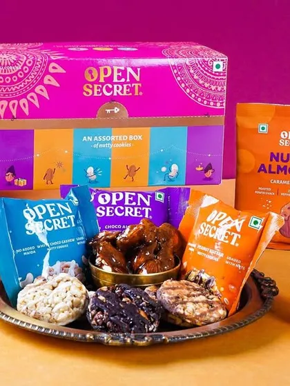 A festive display of Open Secret's healthy Diwali snack hamper. The arrangement on a silver platter with marigold flowers highlights it as a modern, "unjunked" alternative for festive gifting.