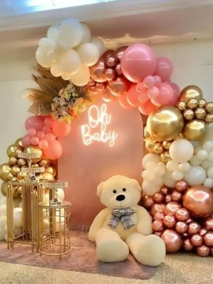 A classic 'Oh Baby' shower setup that is always a hit. This design combines a soft pink backdrop with a trendy neon sign and a lush balloon arch in shades of pink, white, and metallic rose gold.