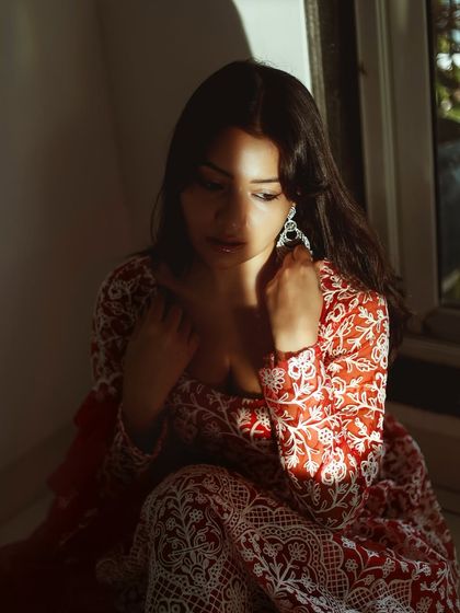 A quiet, introspective moment captured during the shoot. This photo highlights the intricate white embroidery on the red fabric of her traditional dress.