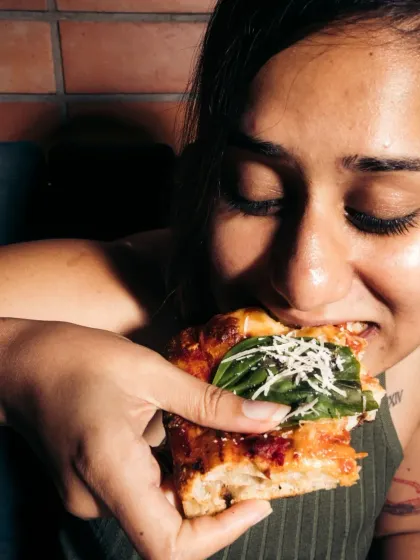 A close-up of a customer taking a bite of pizza, capturing an authentic moment of enjoyment.