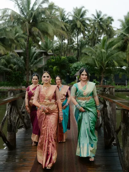 The bride with her bridesmaids, all dressed in gorgeous silk sarees, walking together on a wooden bridge. A beautiful portrait of friendship.