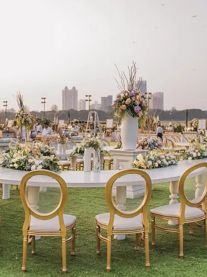 An elegant, long family dining table set up in an open lawn for a reception. This setup encourages intimacy and conversation, all while surrounded by the grand scale of the overall event decor.