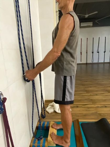 A student using a block under the feet and holding wall ropes to learn the correct foot and leg action. This helps to feel the grounding through the metatarsals.