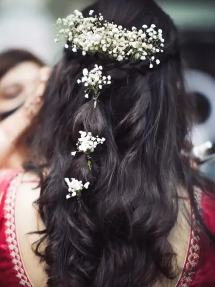 A detailed view of a romantic bridal hairstyle. This half-up style features soft waves and is adorned with delicate baby's breath, creating a look that is both elegant and effortless for an engagement or wedding day.