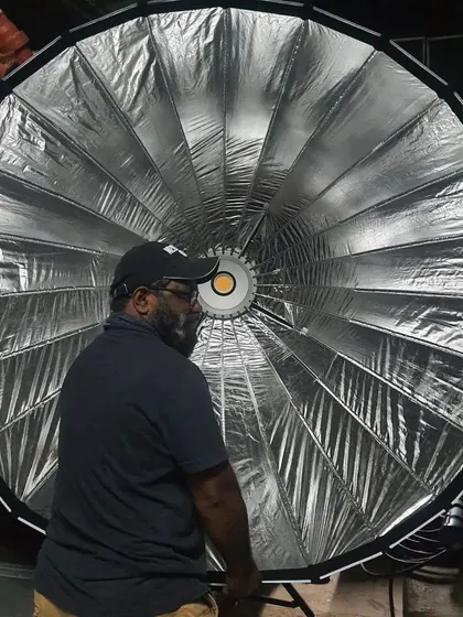 A crew member stands with the powerful 1200-watt Nanlux Evoke 1200 LED light fitted with its large parabolic softbox. This combination creates a strong yet soft source perfect for beauty and interview lighting.
