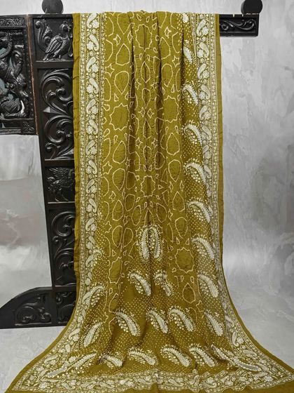 An olive green Bandhani saree with paisley motifs. The intricate tie-dye work creates a beautiful texture and pattern, making it a unique and elegant piece.