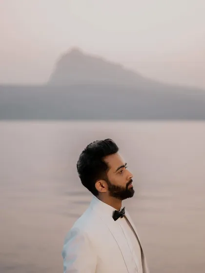 A classic portrait of the groom, Himanshu, set against the calm water and distant mountains at dusk. The soft, ambient light is perfect for capturing pensive and elegant shots.