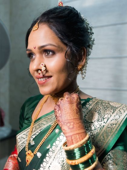 A beautiful portrait of a bride in a green saree, adorned with gold jewelry.
