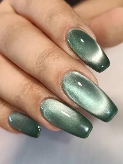 A close-up of a stunning green cat-eye effect on long, square-shaped nails. The magnetic polish creates a deep, velvety finish that shifts from dark to light green.