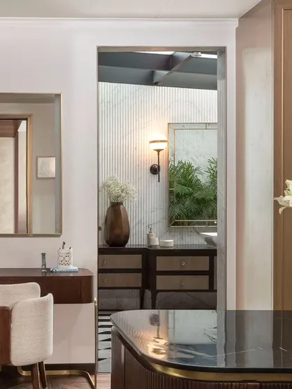 A glimpse from the dressing room into the master bathroom, showcasing a cohesive design journey from one space to the next. The use of mirrors enhances the sense of space and light.