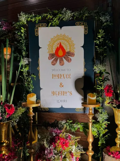 The welcome sign for a couple's first Lohri celebration. We designed a custom sign with a bonfire graphic, framed by lush greenery and flowers, and illuminated by candles for a warm, festive welcome.