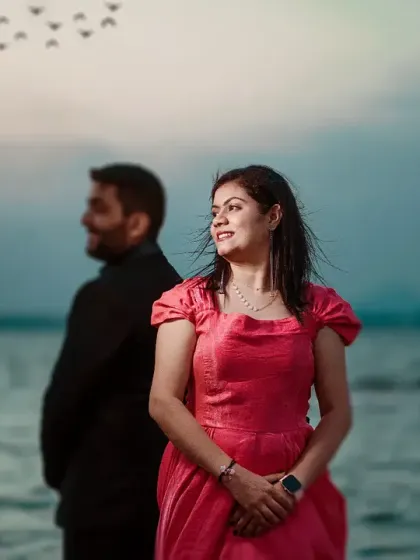 Her serene expression as she looks out over the water, with him standing behind her. The soft, cool tones of the image and the birds in the sky add a peaceful, poetic quality to this pre-wedding portrait.