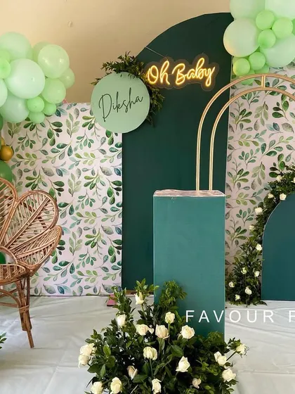A botanical baby shower with a rich, emerald green color palette. We combined a greenery-patterned backdrop with solid green panels, a peacock chair, and an 'Oh Baby' neon sign for a lush and modern look.