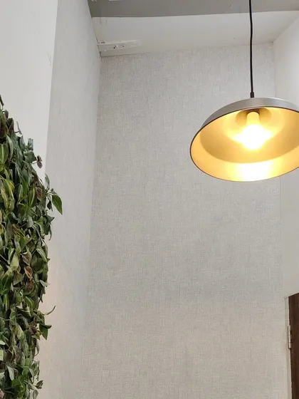 This simple, light-colored wallpaper has a subtle fabric-like texture. It's a versatile choice that adds warmth and sophistication to a wall, pairing well with modern lighting and decor.