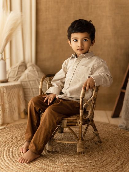 A calm, composed moment of a little boy sitting in a rattan chair. His direct gaze is so captivating.