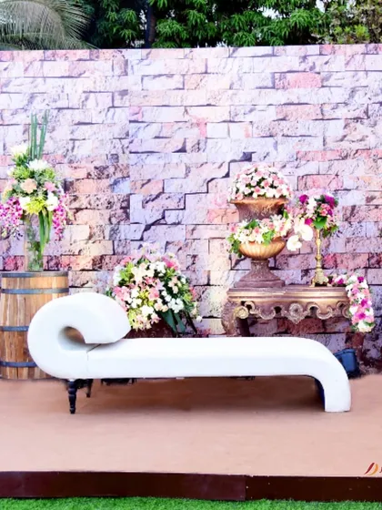 A chic and modern seating arrangement. The unique white chaise lounge is set against a rustic brick wall, flanked by beautiful floral arrangements for a stylish photo corner.