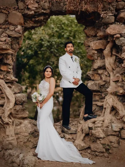 Karen and Abhijeet framed by a natural stone archway in Goa. This shot combines formal wedding attire with a rustic, historic location for a powerful, editorial-style portrait.