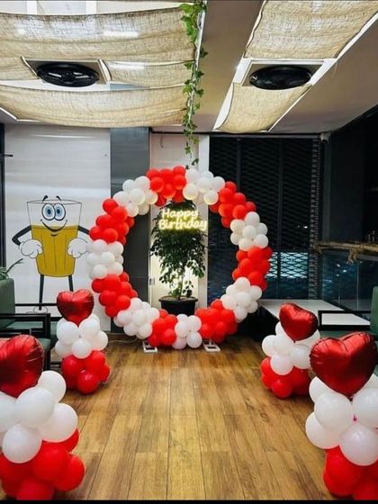 This birthday decoration was set up in a cafe, showing how I can adapt my designs to any space. It features a circular balloon arch in red and white with a 'Happy Birthday' neon sign at the center.