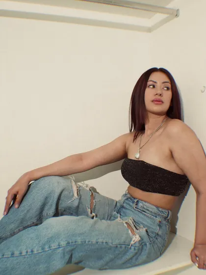 A moody shot sitting in a wardrobe, wearing a black sequin bandeau with ripped jeans.