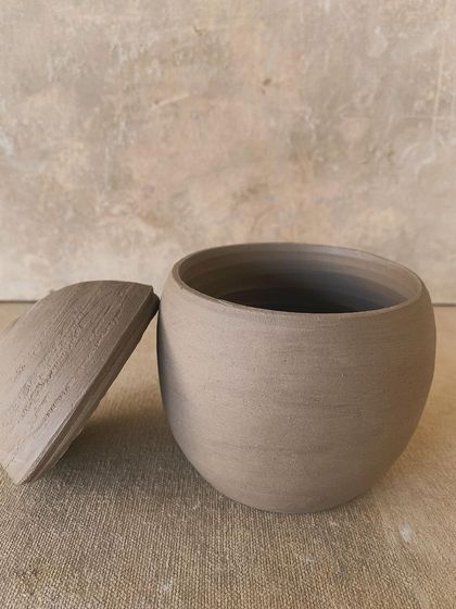 A perfectly rounded, unglazed jar and lid. The simplicity of the form highlights the natural beauty and color of the raw clay.