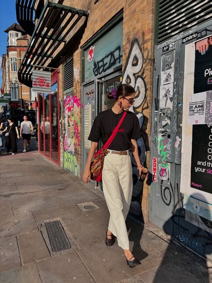A candid street style moment in London. A simple black tee, white pants, and a pop of red in the bag is my go-to formula for a cool, effortless city look.