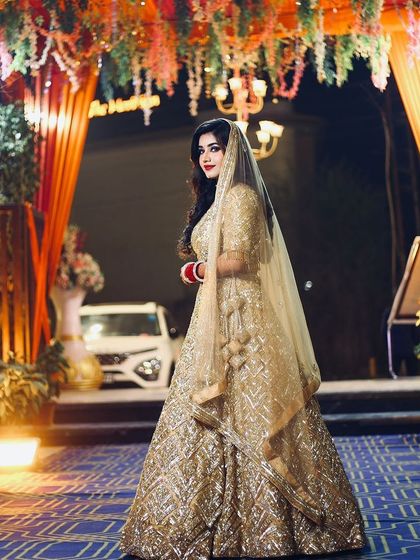 A full-length shot of the reception bride at the venue. The golden lehenga and glowing makeup look magnificent under the lights.