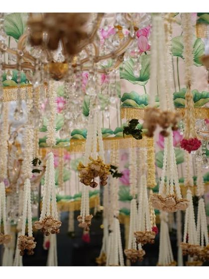 A stunning ceiling of hanging flowers, chandeliers, and lotus-printed drapes, creating a multi-layered and culturally rich installation.