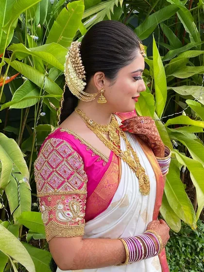 This bride is glowing in her complete Muhurtham look. The traditional braid with flowers and jewellery perfectly complements her bright pink and white saree and radiant smile.