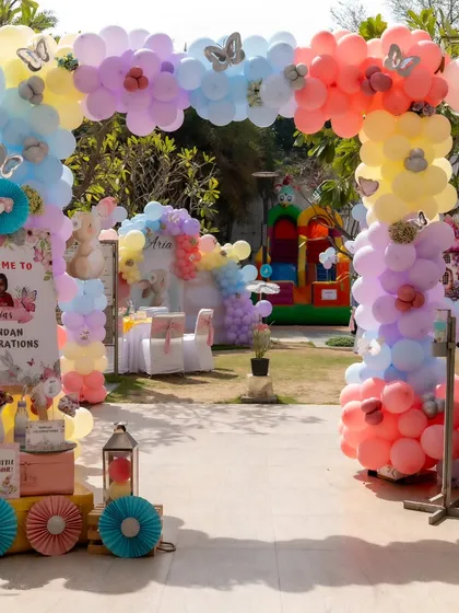 A wide view of the entrance to the pastel-themed Mundan celebration. A beautiful balloon arch frames the view into the garden, where a bouncy castle awaits the kids.