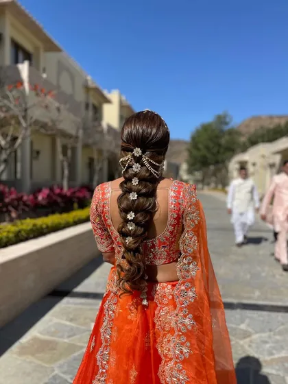 A full-length view of a bride with a long, accessorized braid against a beautiful outdoor backdrop. This shows how a statement braid can complete a vibrant wedding look.
