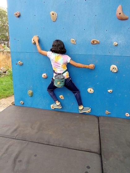 A participant with a chalk bag scales the bouldering wall, practicing moves before tackling natural rock formations.