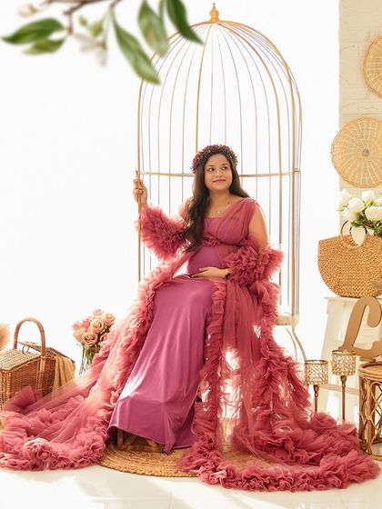 A serene solo portrait of the mom-to-be seated in our golden birdcage swing. The dusty rose ruffled gown drapes beautifully in our bright and airy boho set.