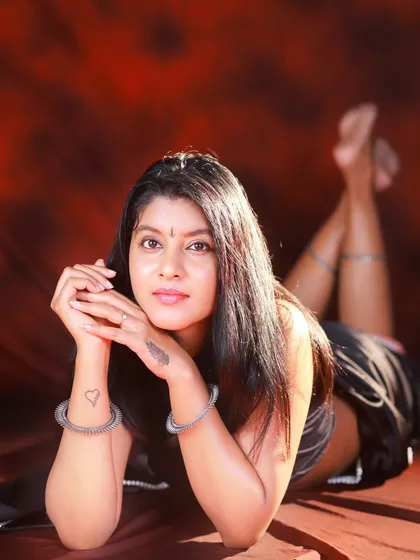 A relaxed and intimate portrait from a studio session. The model is wearing a modern black saree with a halter neck, and the warm lighting creates a soft, inviting mood.