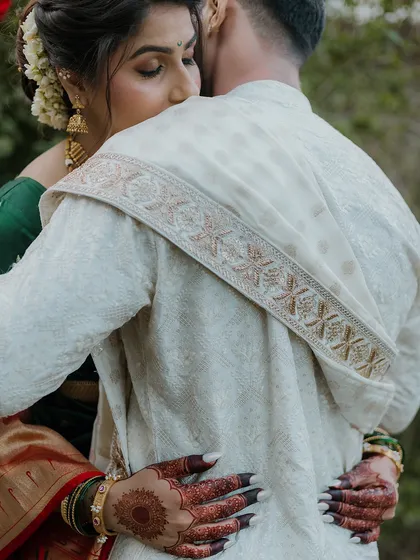 An intimate embrace captured from behind the groom. This angle focuses on the bride's expression and the beautiful details of her henna and green bangles, telling a story of love and trust.